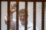 Egypt's deposed Islamist president Mohamed Morsi waves inside the defendants cage during a trial at the police academy in Cairo on December 7, 2014. An Egyptian court sentenced to death four members of the blacklisted Muslim Brotherhood over the killing of protesters who stormed the group's Cairo headquarters in June last year. Decisions on 14 other defendants in the case, including Muslim Brotherhood chief Mohamed Badie and his deputies Khairat al-Shater and Saad al-Katatni, will be made at the next hearing on February 28, the official said. AFP PHOTO / AHMED RAMADAN